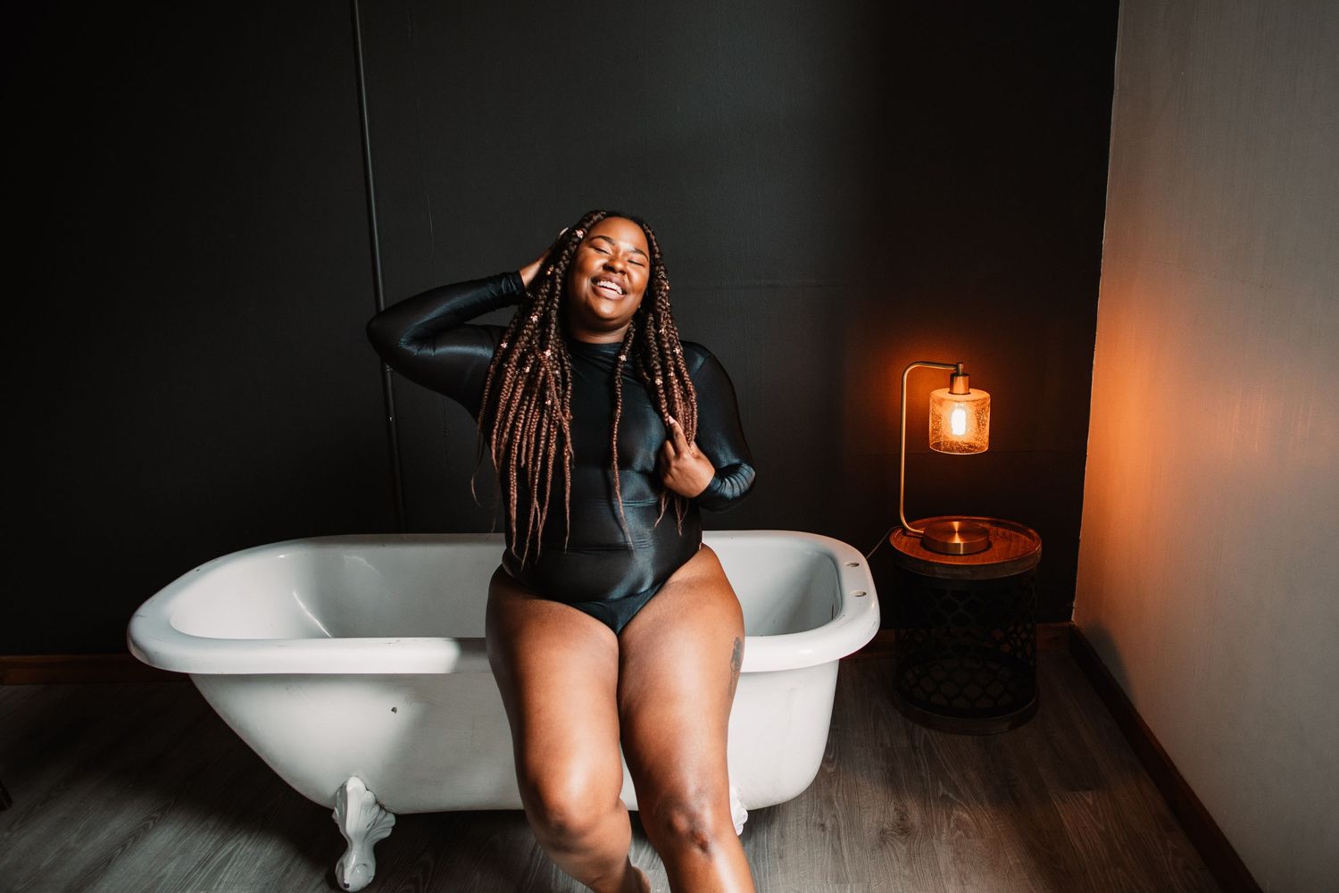 Woman with long braids posing in vintage bathtub with ambient lighting.