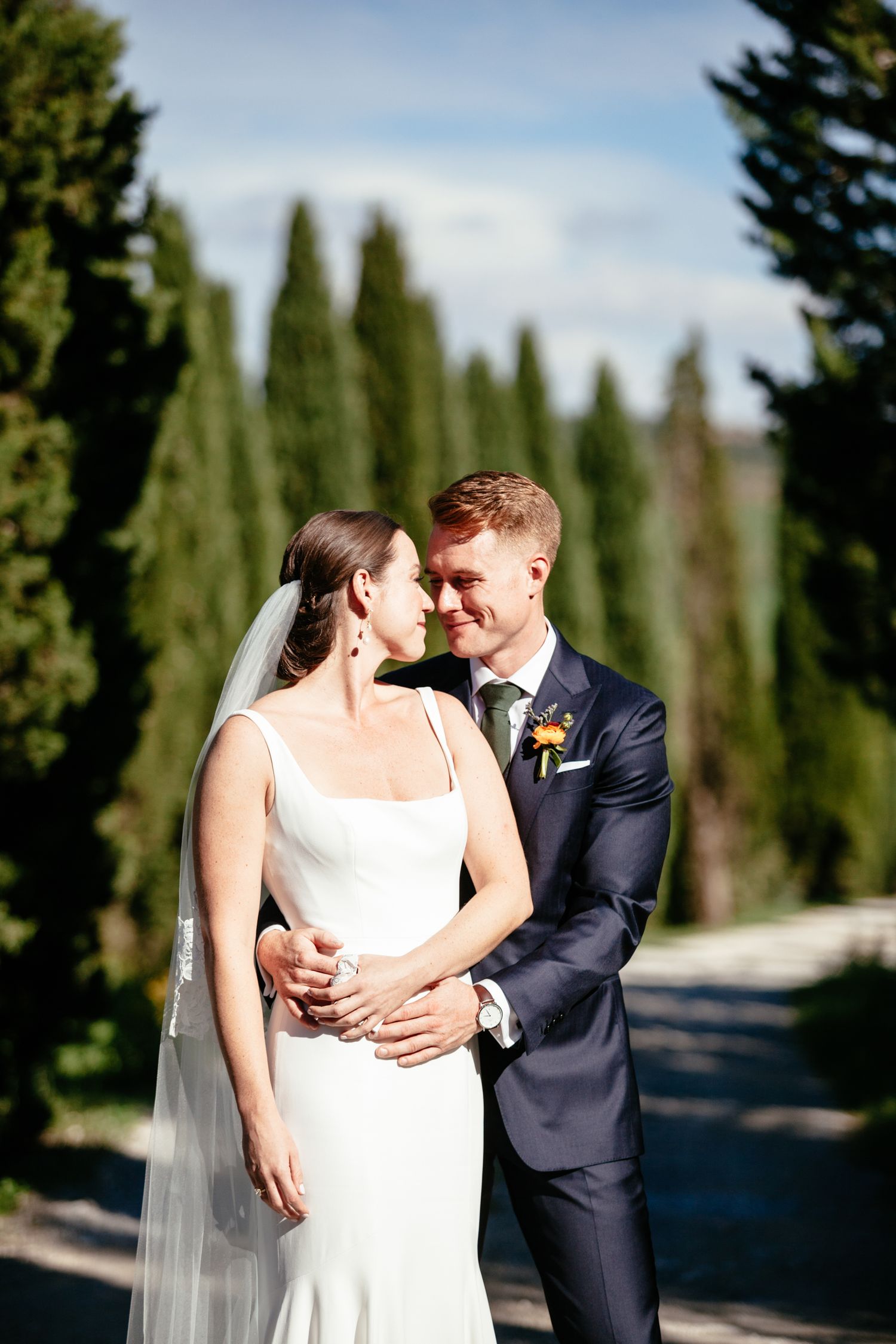 Bride and groom photographed along a tree lined avenue in Tuscany before their wedding.