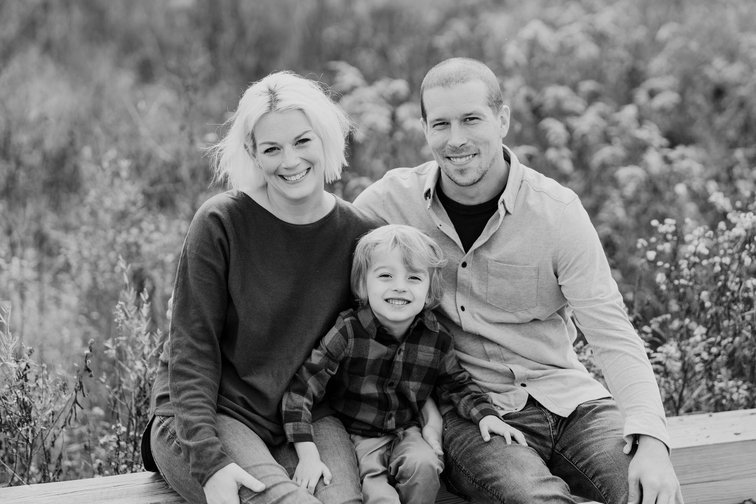 A casual outdoor family portrait taken in a field with flowering plants.