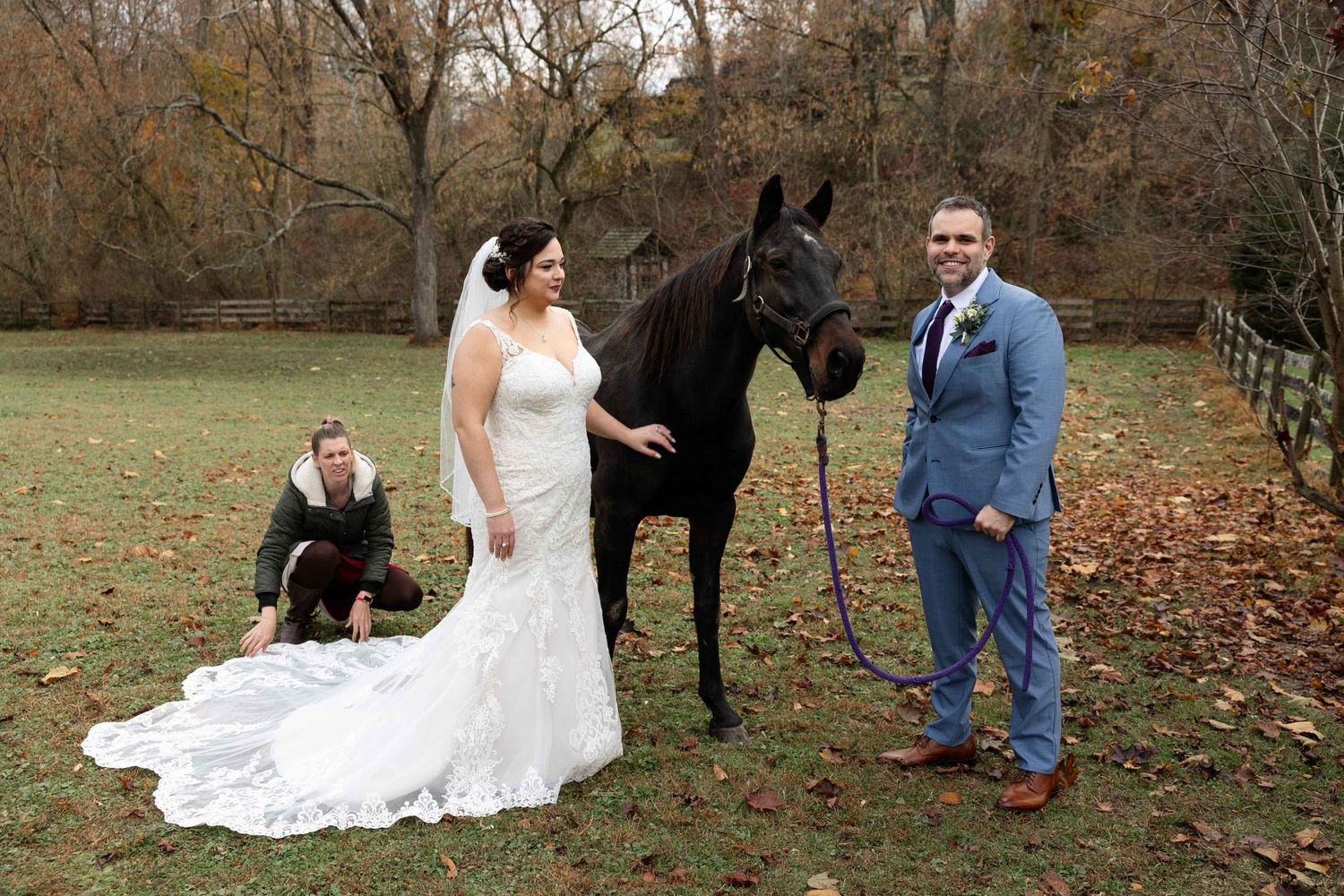 Wedding photo with black horse in autumn field featuring long white lace gown.