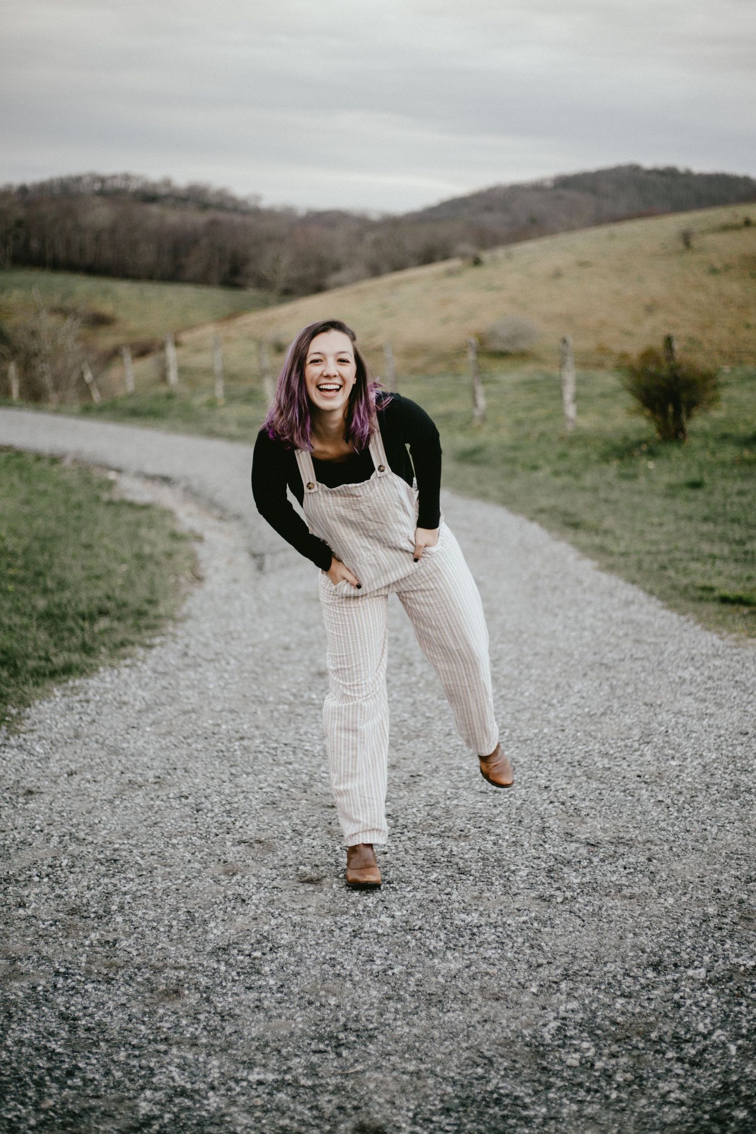 Person in white overalls laughs while standing on a rural mountain path.
