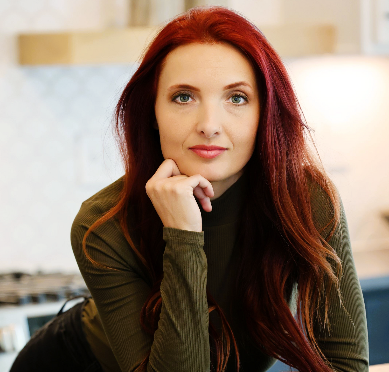 Professional realty portrait featuring vibrant red hair and olive green top against a light background.