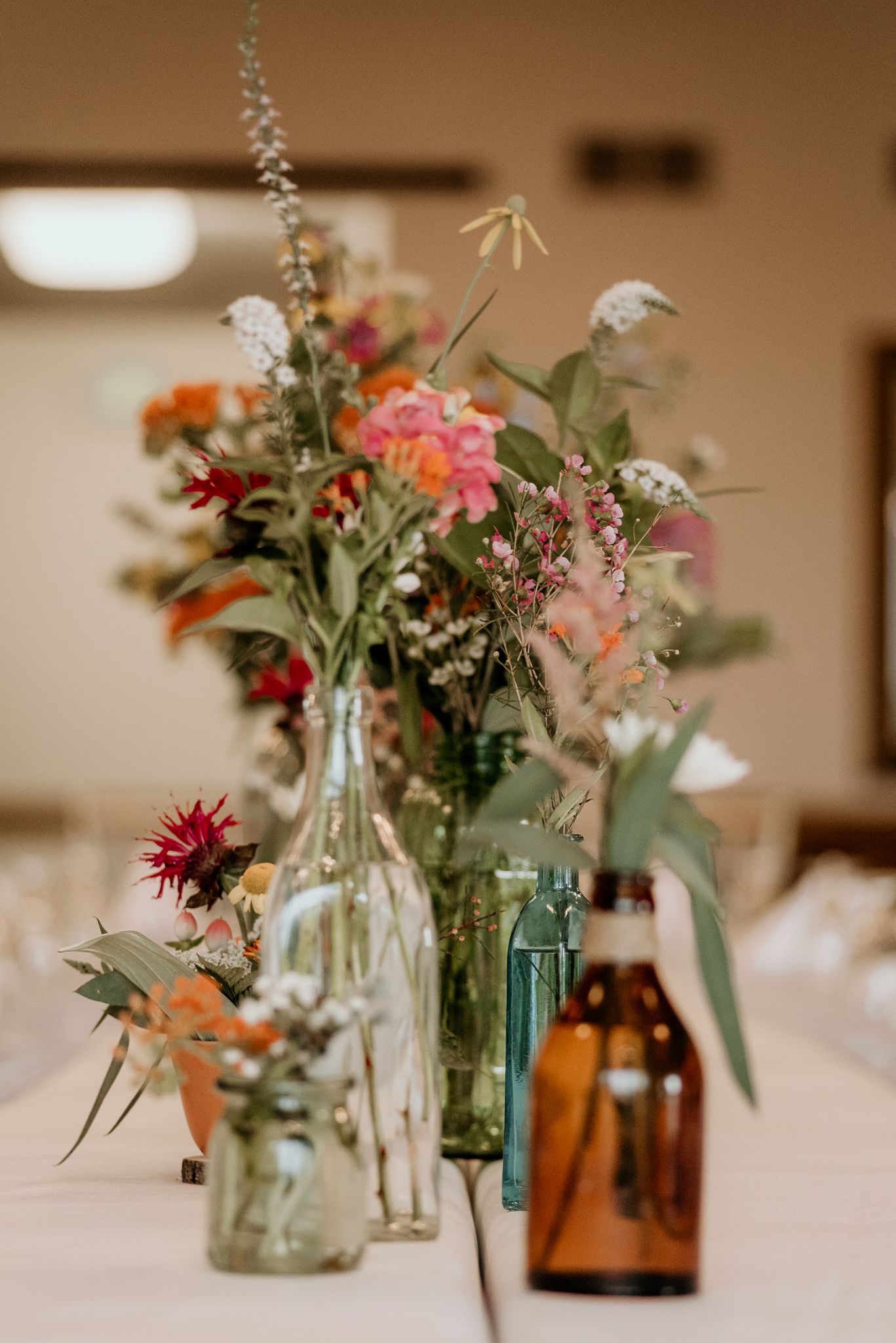 Wildflower arrangements in mixed glass bottles create rustic centerpiece display.