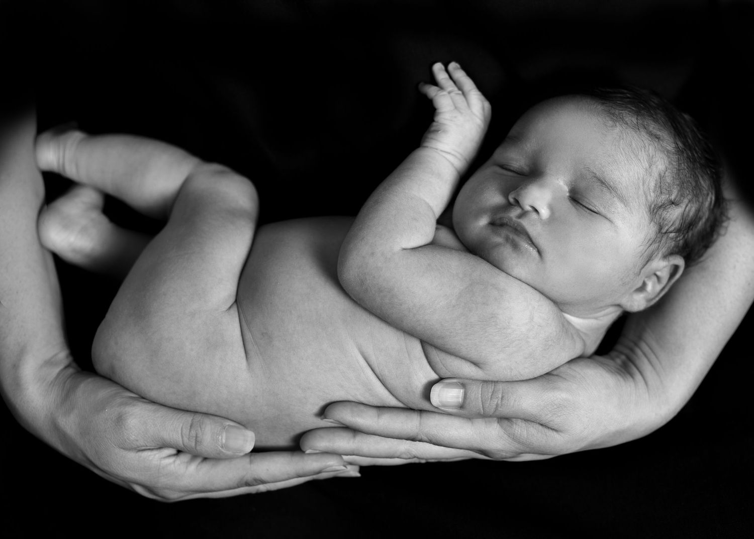 A peaceful newborn baby resting in gentle adult hands, captured in black and white.