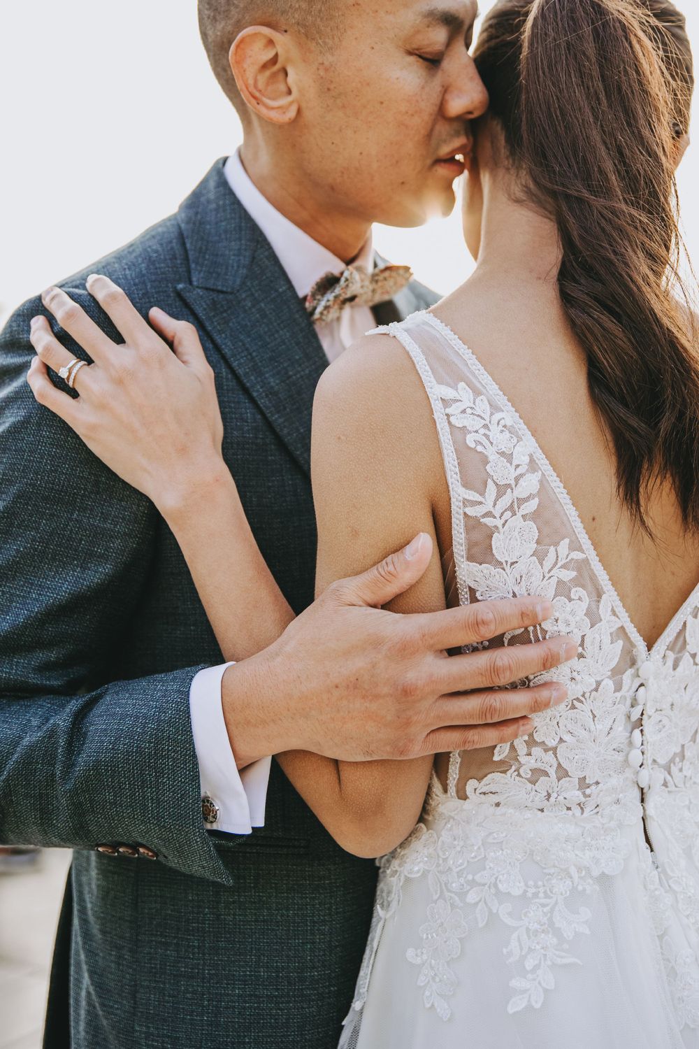 Intimate close-up of wedding couple embracing, showing delicate lace details of the bride's dress.