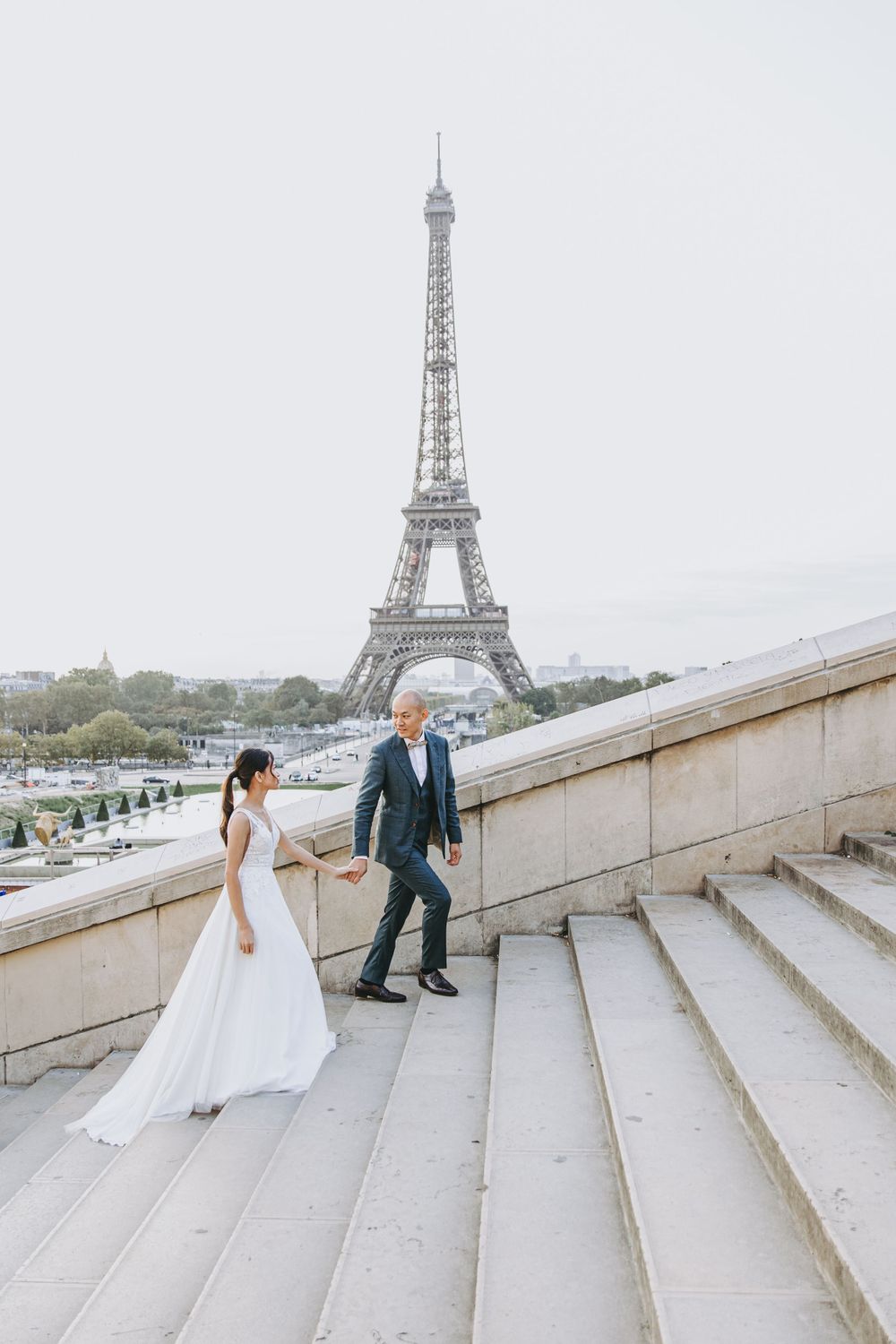 Couple walking up stone steps with the Eiffel Tower visible in the background on their wedding day.