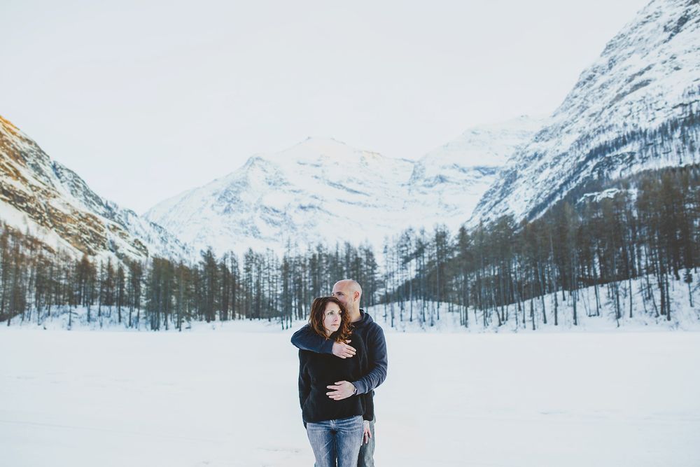 Couple shares intimate moment against dramatic snow-capped mountain backdrop.
