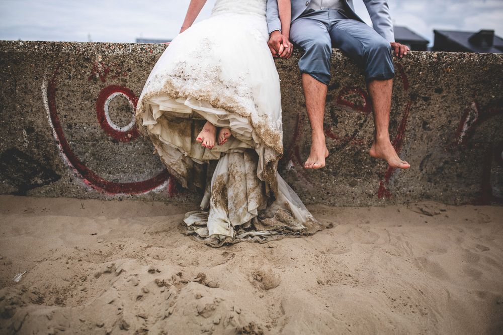 Close-up of bare feet and white wedding dress hem on sandy beach.