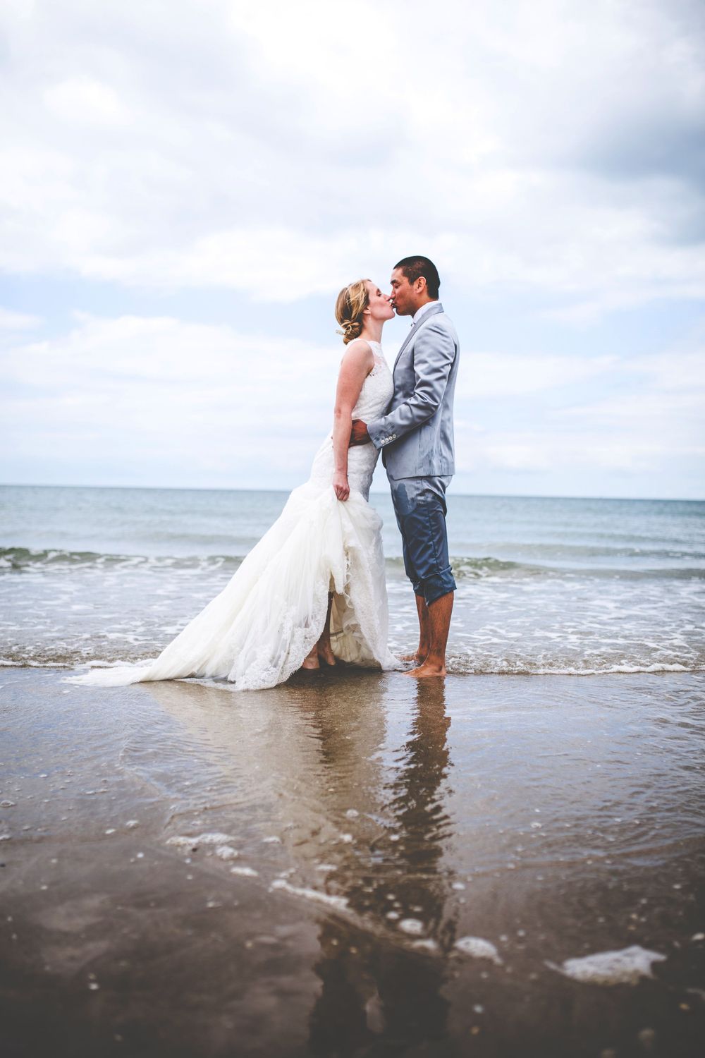 A couple shares an intimate moment while standing in shallow ocean waves at the beach.