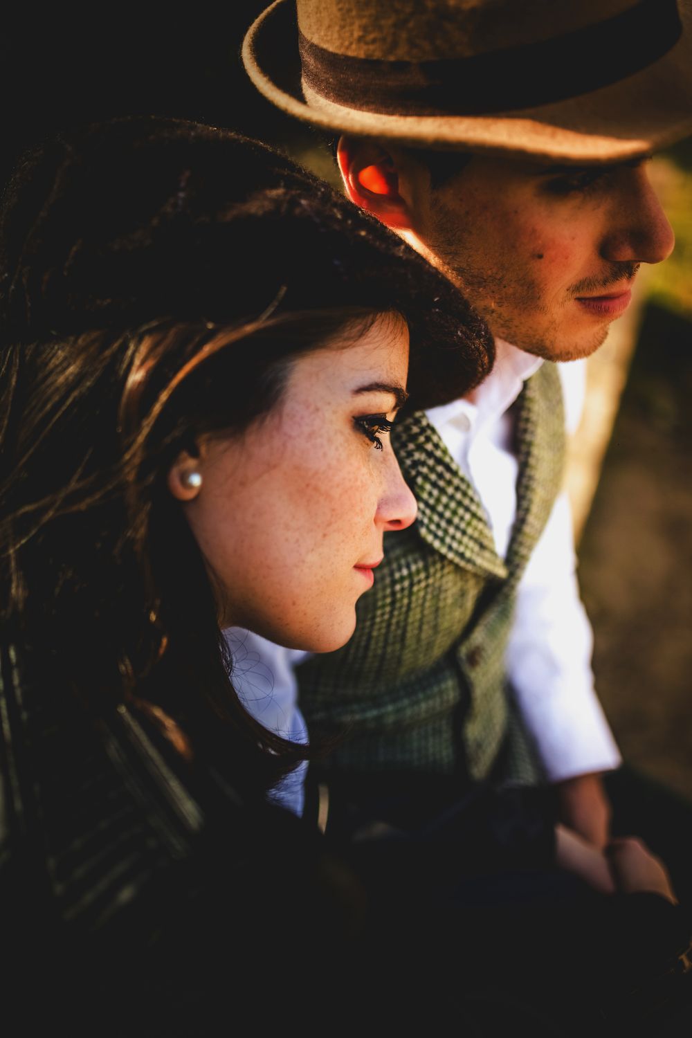 Intimate close-up portrait of two people wearing western hats in warm golden lighting.