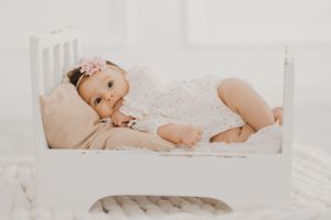 A baby in white lace clothing rests in a small white wooden bed.