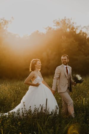 Wedding couple posing in golden field during sunset with bride in white gown.