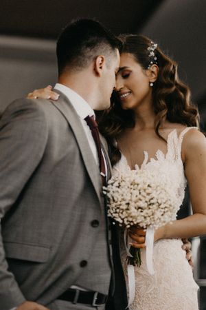 Intimate moment between bride and groom sharing close embrace with bouquet.