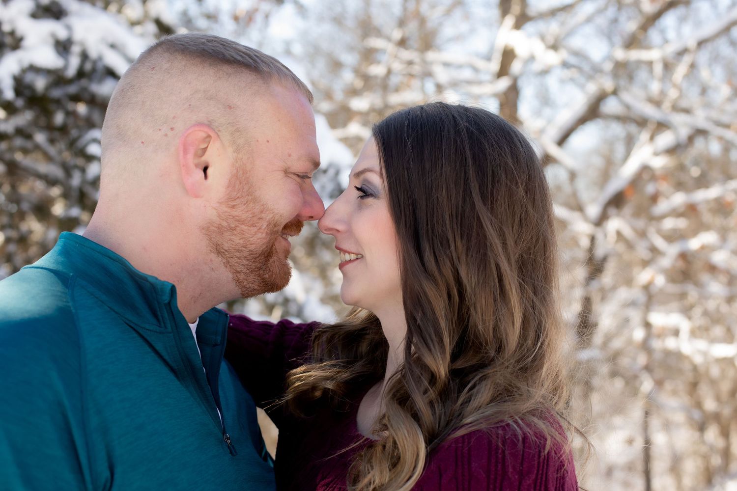 Intimate moment between couple sharing laughter against snowy winter forest backdrop.