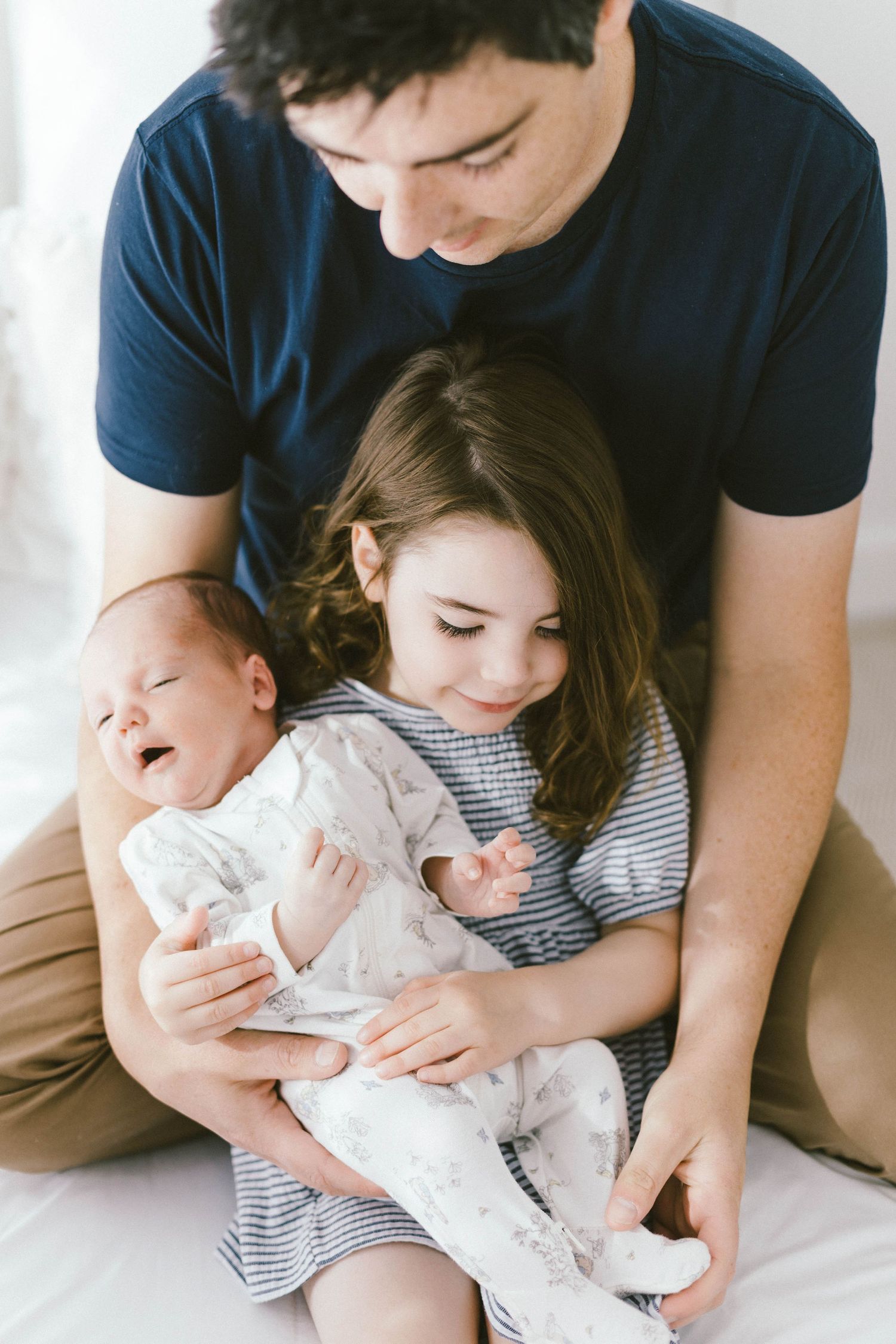 Family snuggling together with newborn baby on white couch.