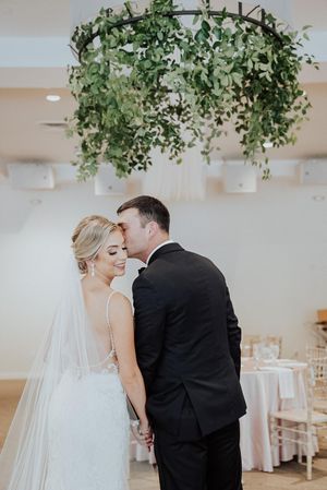 A romantic moment under a hanging greenery installation at an elegant wedding reception.