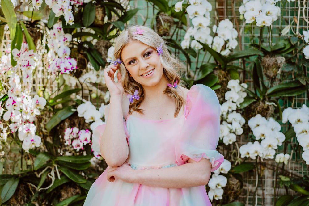 A whimsical pink and blue dress is captured among blooming white orchids in a garden setting.