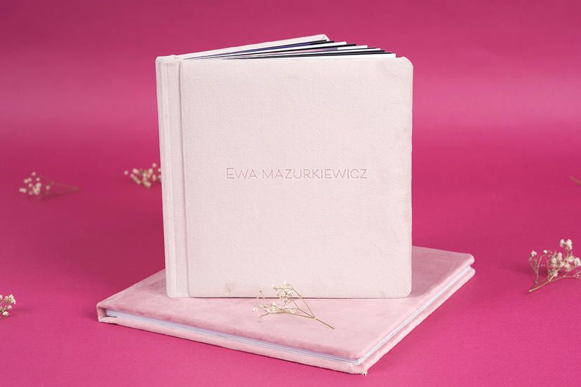 White leather photo album book on pink background with delicate dried flowers.