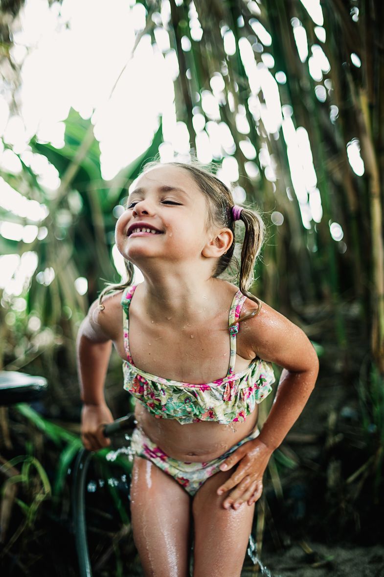 Happy young girl in floral bikini with eyes closed smiling under tropical palm trees.