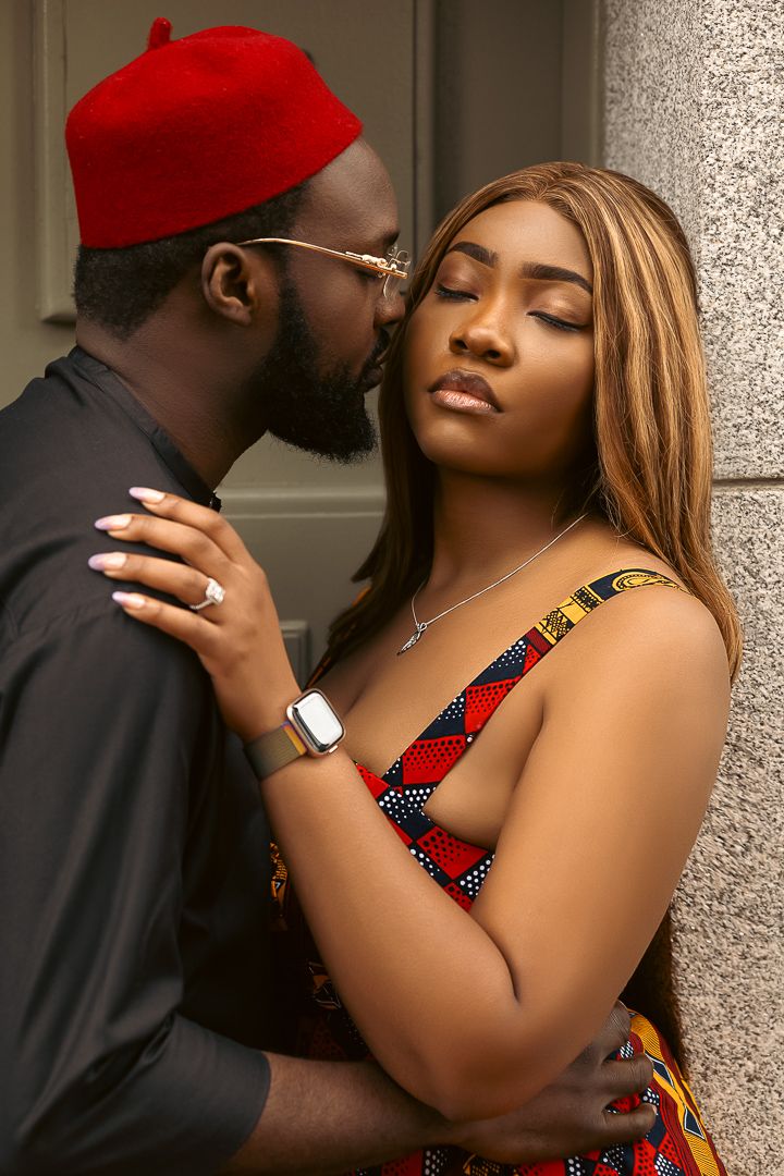 Intimate portrait of couple in traditional African attire embracing against grey wall.