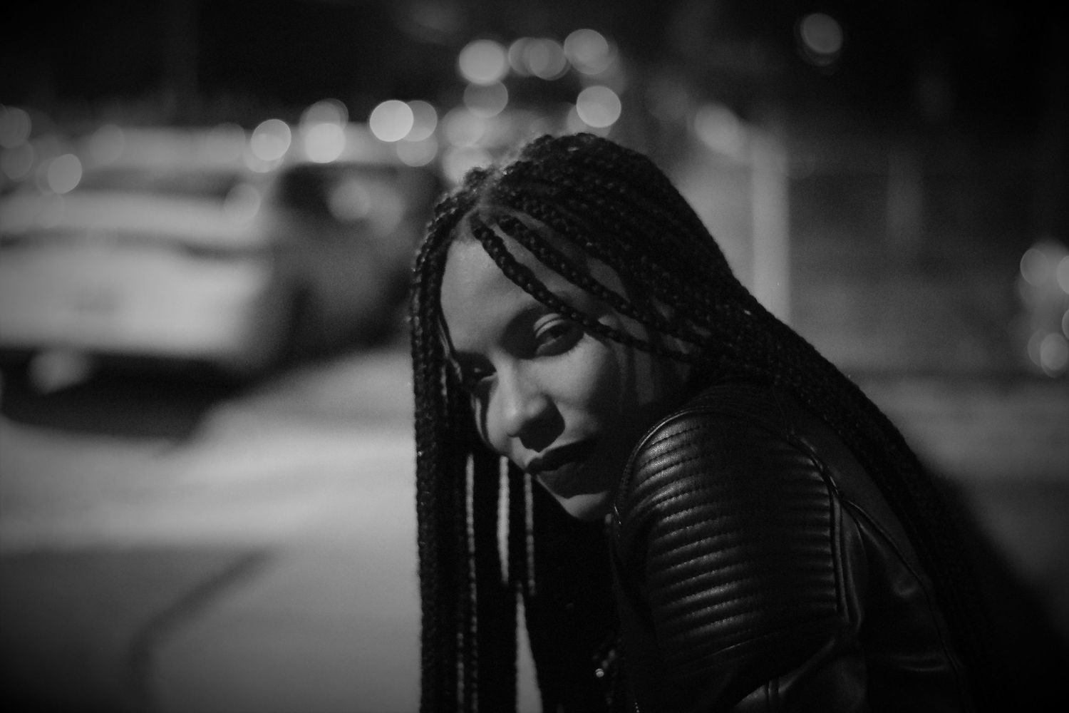 Artistic black and white portrait of a beautiful woman showing long braids in moody nighttime setting.