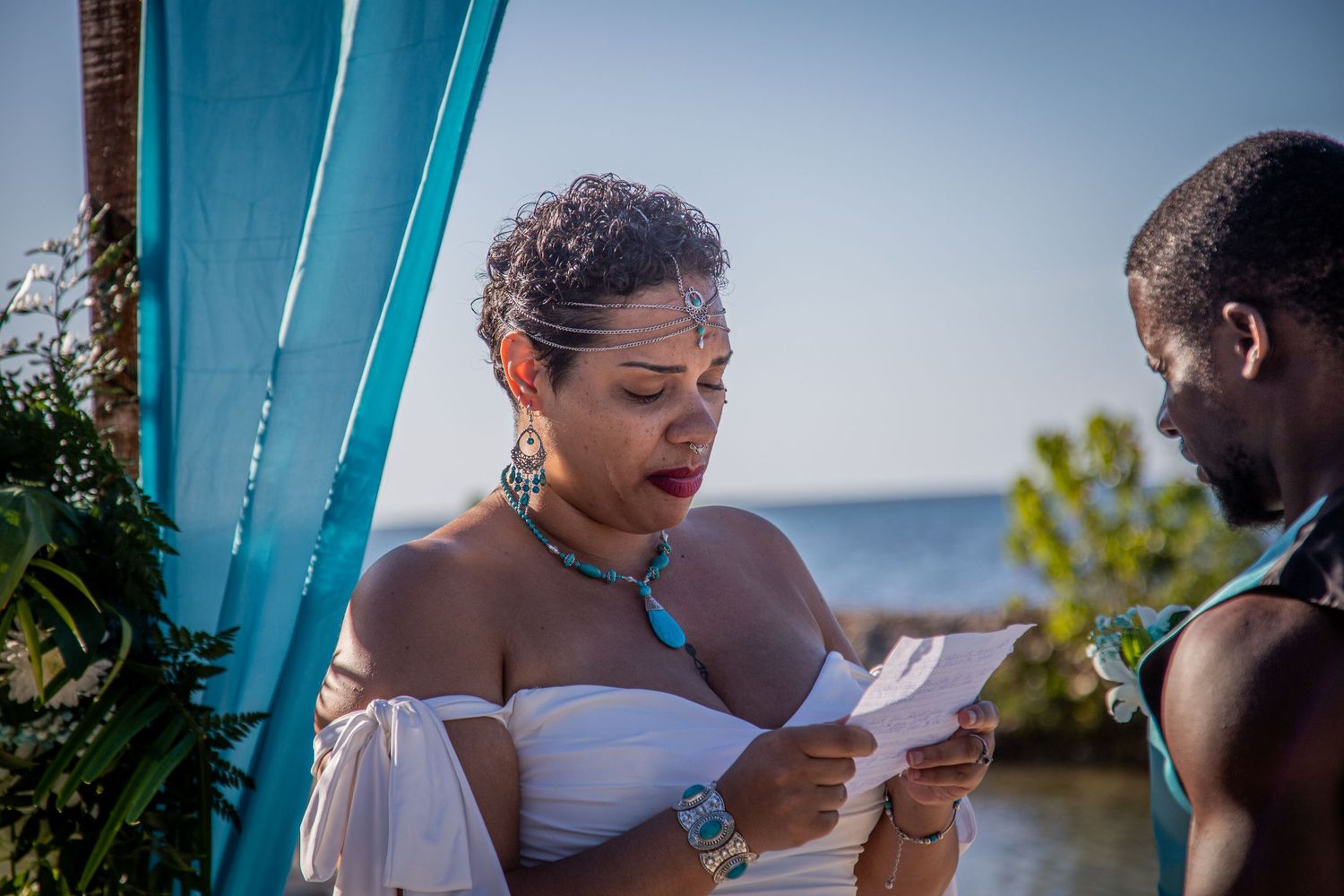 Emotional beach wedding ceremony with couple exchanging vows under turquoise arch.