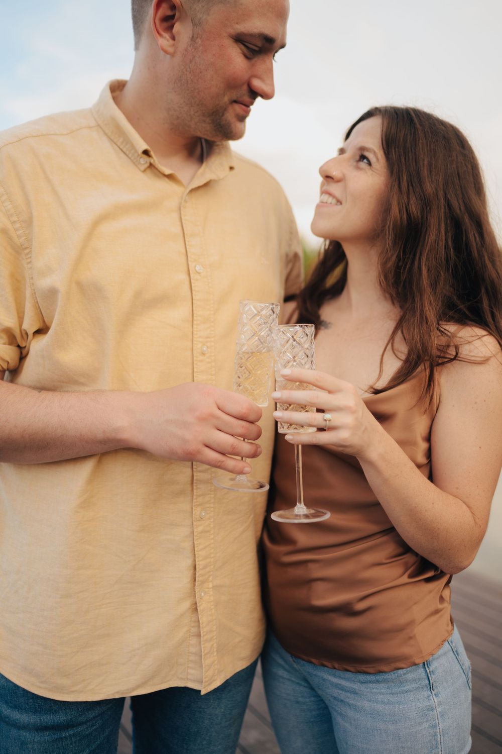 Happy couple toasting with champagne glasses outdoors during golden hour.