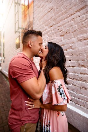 Romantic couple sharing intimate moment against brick wall in urban setting.