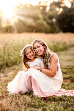 Mother and daughter sharing tender moment in golden field at sunset wearing flowy dresses.