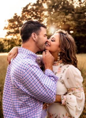 A romantic embrace captured during a golden hour photoshoot in a rustic field setting.