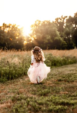 Young girl in flowing pink dress running through sunlit meadow at golden hour.