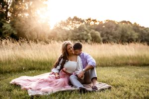 A couple sits on a blanket in a sunlit meadow during golden hour.
