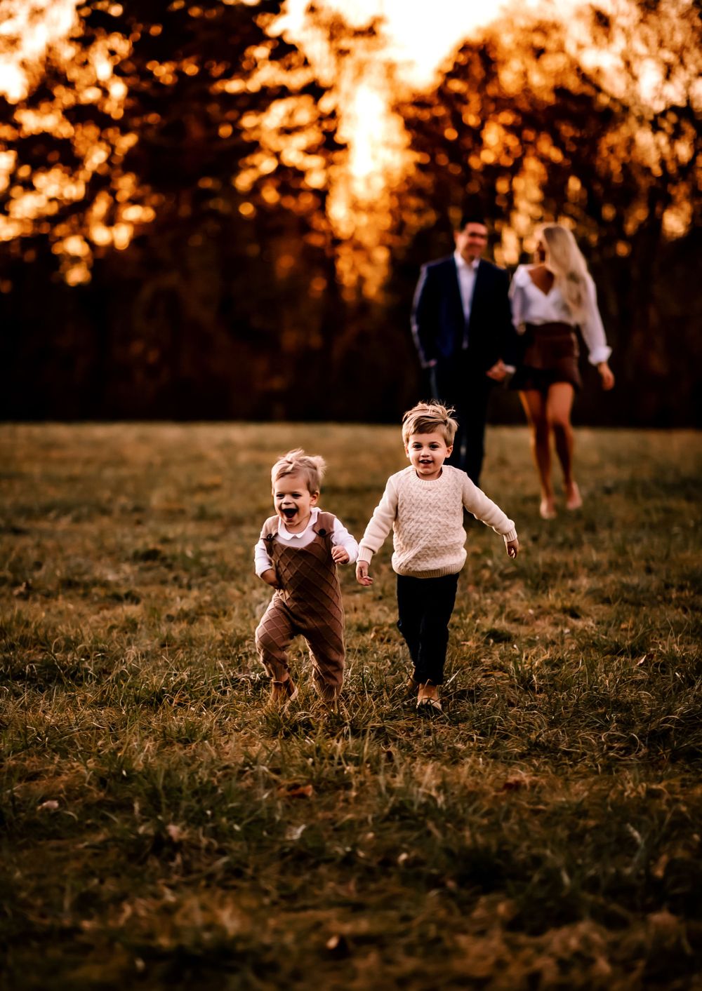 Children running joyfully through a field at sunset while adults watch from behind.