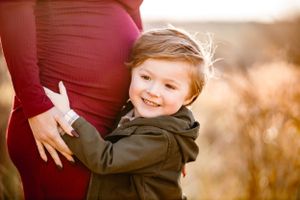 Young child hugging a pregnant woman's belly in warm autumn light.