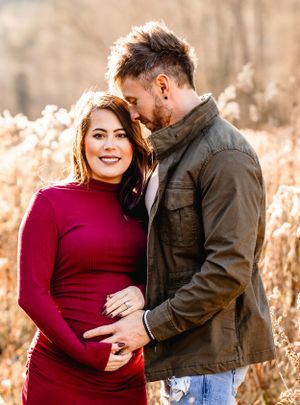 Expectant couple sharing an intimate moment in a field of dried grass at sunset.