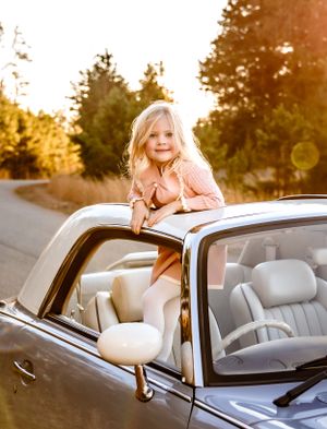 Adventurous pose standing through the sunroof of a classic car at sunset.