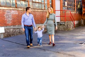 A family walks together holding hands of a toddler along an urban brick building exterior.
