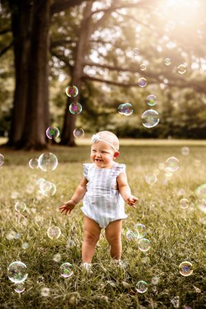 Baby in striped romper delightedly playing with soap bubbles in a sunlit garden setting.