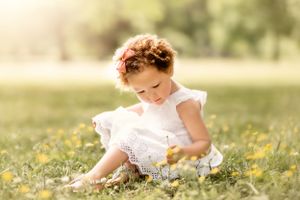 Child in white dress picking flowers in sunny meadow.