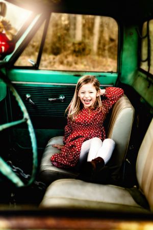 Inside a mint green vintage car, someone in a red polka dot dress laughs while sitting on tan leather seats.