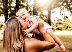 Playful mother-child moment captured in sunlit outdoor setting.