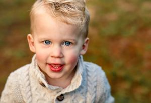 A close-up portrait of a toddler wearing a beige sweater smiling at the camera.
