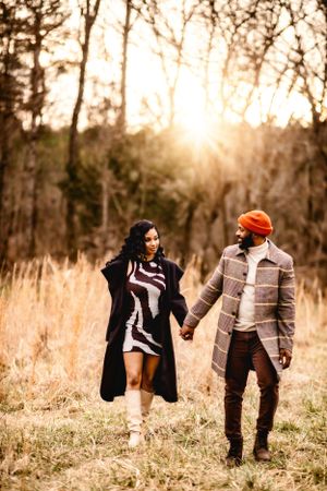 A romantic couple strolls hand in hand through tall grass at sunset.