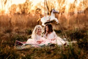 Two people in pink dresses sitting on blanket during golden sunset.