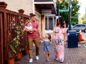 Family walking together on urban sidewalk with flowering fence.