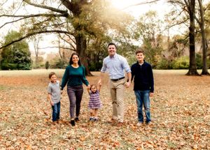 Family of five walking together through autumn leaves in a park setting.