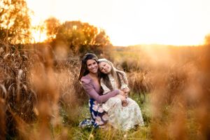 Two people sitting together in tall grass at sunset with warm golden light.