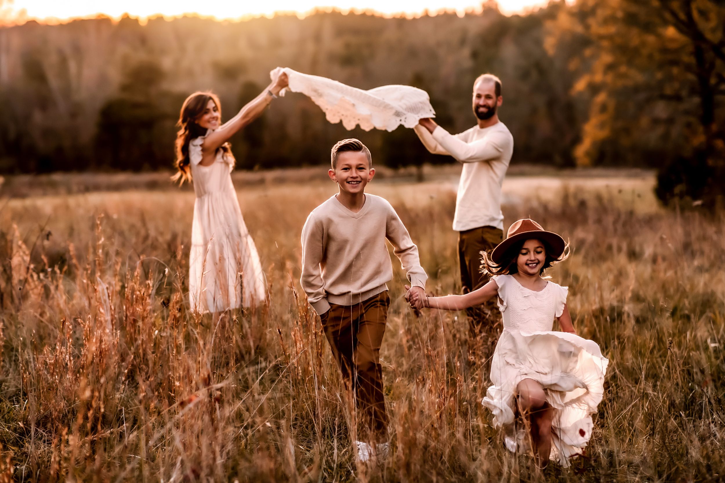 Playful family moment captured in sunset-lit meadow with flowing dresses.