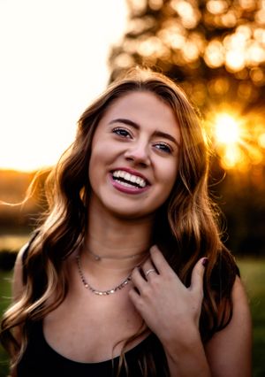 Portrait of a young woman smiling in golden sunlight wearing a necklace and black top.
