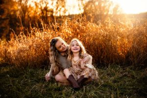 Two people laughing together in tall grass during golden sunset.